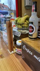 Ein Verkaufsstand mit Bananen in einem Korb und verschiedenen Zutaten für Crêpes. Auf dem Tisch stehen Nutella und andere Saucen.
