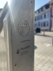 Ein modernes, metallisches Schild mit einem Wasserhahn-Symbol. Es zeigt Informationen über öffentliche Trinkwasserstellen in Rheinfels.