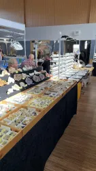 Ein Markt mit verschiedenen Mineralien und Steinen auf einem Tisch. Im Hintergrund sind Besucher zu sehen, die sich die Ausstellung ansehen.