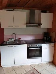 Eine moderne Küche mit weißen Schränken und einem Herd. Die Wände sind in sanften Farben gehalten, und eine Spüle ist vorhanden.