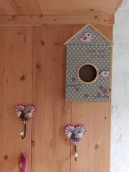 Ein dekoratives Vogelhaus mit Punkten und einem kleinen Vogel auf der Vorderseite. Daneben hängen zwei hängende Herzen aus Holz.