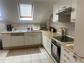Eine moderne Küche mit heller Ausstattung und vielen Geräten. Der Raum ist sauber und gut organisiert, mit einem Fenster, das Tageslicht hereinlässt.