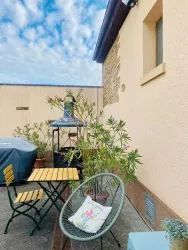 Ein gemütlicher Außenbereich mit einem Tisch, Stühlen und einer Pflanze. Im Hintergrund sind eine Gartenlaube und ein blauer Himmel zu sehen.