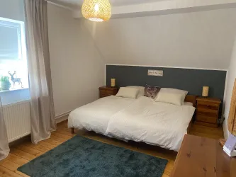 Ein gemütliches Schlafzimmer mit einem Doppelbett und Holzmöbeln. Der Raum hat einen warmen Holzboden und eine sanfte Beleuchtung.