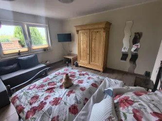 Ein gemütliches Schlafzimmer mit einem Bett auf einer Blumenbettwäsche und einem Schrank aus Holz. Im Raum steht ein Sofa und ein Fernseher ist an der Wand befestigt.