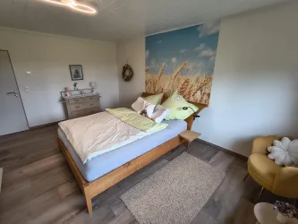 Ein gemütliches Schlafzimmer mit einem großen Bett und schönen Kissen. An der Wand ist ein Bild von einem Getreidefeld, das für eine entspannende Atmosphäre sorgt.
