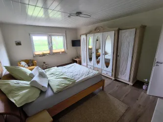 Ein gemütliches Schlafzimmer mit einem großen Bett und hellen Kissen. Der Raum ist neutral eingerichtet und hat einen großen Kleiderschrank.
