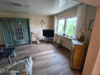 Ein gemütliches Wohnzimmer mit einem Fernseher. Helle Fenster sorgen für viel Tageslicht und eine einladende Atmosphäre.