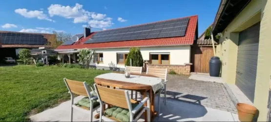 Ein modernes Haus mit Solarpanelen auf dem Dach. Vor dem Haus befindet sich ein gemütlicher Essbereich im Freien.