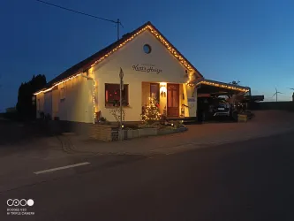 Ein hübsches Haus, festlich dekoriert mit Lichtern und einem Weihnachtsbaum. Die Dämmerung sorgt für eine gemütliche Atmosphäre.
