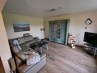 Ein gemütliches Wohnzimmer mit einer modernen Couch und einem Fernseher. Der Raum hat ein gemütliches Ambiente.