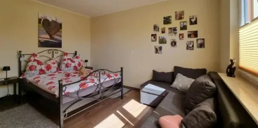 Ein gemütliches Zimmer mit einem Bett und einer Couch. An der Wand sind zahlreiche Fotos angebracht.