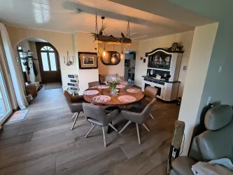 Ein einladender Essbereich mit einem runden Tisch und stilvollen Stühlen. Das Interieur ist hell und freundlich, mit einer großen Fensterfront und dekorativen Details.