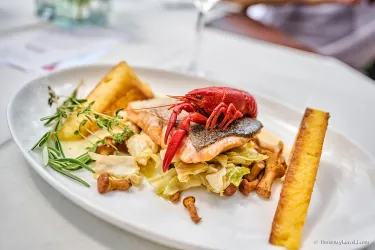 Ein dekorierter Teller mit gegrilltem Fisch, einer Garnele und Beilagen aus Gemüse und Kartoffeln. Das Gericht ist frisch und ansprechend angerichtet.