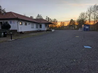 Ein ruhiger Parkplatz vor einem Gebäude bei Sonnenuntergang. Die Umgebung ist ruhig mit Bäumen im Hintergrund.