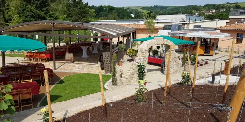 Ein wunderschöner Gartenbereich mit einer überdachten Terrasse und mehreren Tischen. Im Hintergrund sind grüne Hügel und einladende Sitzgelegenheiten zu sehen.