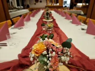 Ein festlich gedeckter Tisch mit rosa Servietten und einer zentralen Blumendekoration. Der Tisch ist hübsch dekoriert, ideal für eine Feier oder ein Bankett.