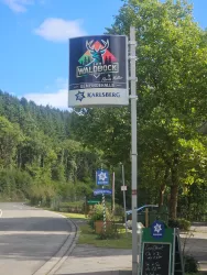 Ein Schild für das Walddock und die Gemeindehalle ist sichtbar. Umgeben von grünen Bäumen und einer ruhigen Landschaft.