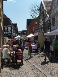 Ein belebter Marktplatz mit vielen Menschen und Ständen. Die Atmosphäre ist freundlich und einladend, umgeben von historischen Gebäuden.