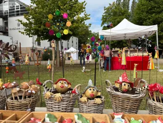 Ein farbenfroher Markt mit handgefertigten Skulpturen aus Ton und Holz. Im Hintergrund sind Stände mit Dekorationen und Besuchern zu sehen.