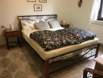 Ein gemütliches Schlafzimmer mit einem großen Bett und einer bunten Bettdecke. Neben dem Bett stehen zwei Nachttische und ein Teppich liegt auf dem Boden.