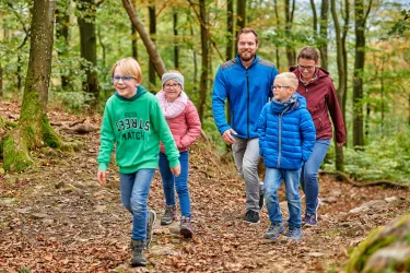 Familie mit drei Kindern wandert durch den Wald.