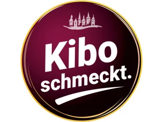 Ein runder, lila Logo mit dem Text "Kibo schmeckt." in großen, weißen Buchstaben. Darüber ist eine Abbildung von Gebäuden zu sehen.