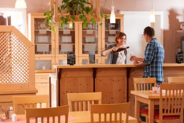 Ein gemütliches Restaurant mit Holzinterieur. Eine Bedienung serviert einem Gast am Empfangstresen.