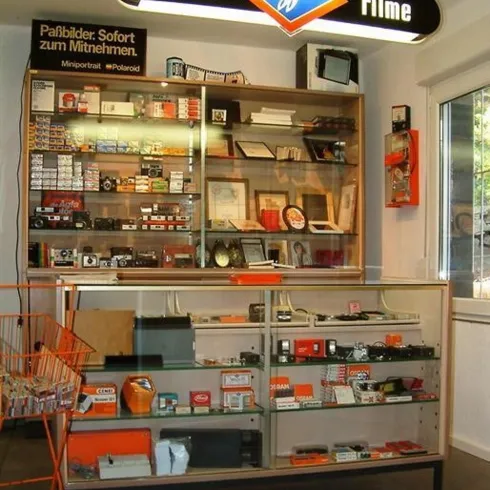 Ein Verkaufsraum mit einem Glasregal voller Kameras und Filme. Über dem Regal hängt ein Schild mit der Aufschrift "Cameras Filme".