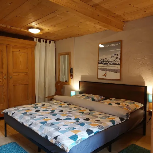 Ein gemütliches Schlafzimmer mit einem großen Doppelbett und bunten Bettdecken. Holzvertäfelung und ein Kleiderschrank schaffen eine warme Atmosphäre.