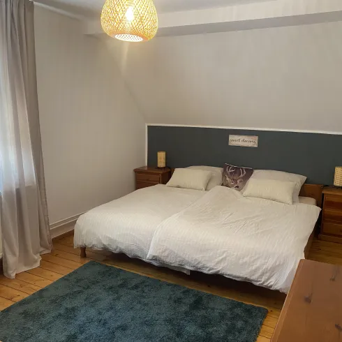 Ein gemütliches Schlafzimmer mit einem Doppelbett und Holzmöbeln. Der Raum hat einen warmen Holzboden und eine sanfte Beleuchtung.