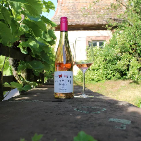 Ein Flasche Roséwein steht auf einem Tisch neben einem Weinglas. Im Hintergrund ist ein malerischer Garten mit viel Grün zu sehen.