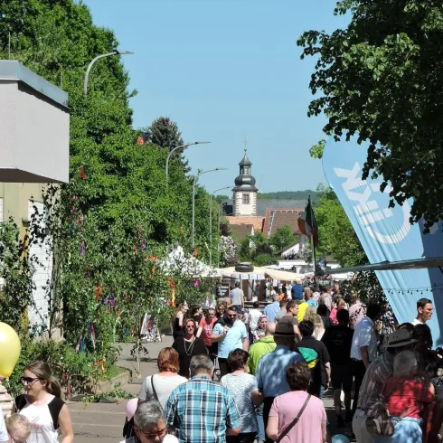 Eine belebte Straße mit vielen Menschen und Ständen. Im Hintergrund ist ein Kirchturm sichtbar.