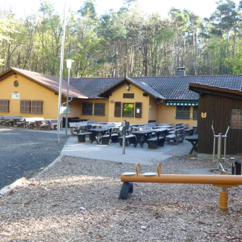Ein gemütliches Gebäude im Wald mit mehreren Sitzplätzen im Freien. Es ist eine einladende Umgebung, ideal für Outdoor-Aktivitäten.