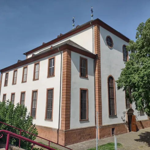 Ein historisches Gebäude mit einer weißen Fassade und großen Fenstern. Umgeben von Bäumen und einem kleinen Garten.