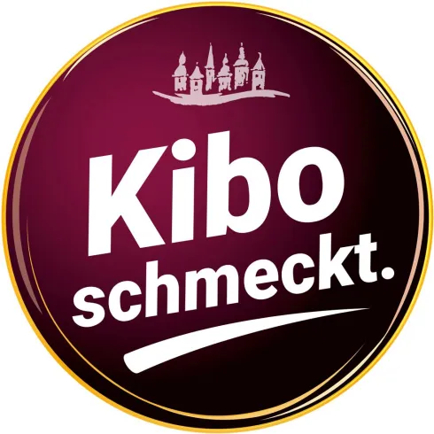 Ein rundes Logo in dunklem Violett, das den Text "Kibo schmeckt." zeigt. Oben sind stilisierte Gebäude abgebildet.
